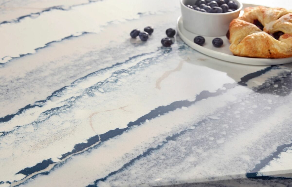 Close-up view of Cambria Inverness Bristol Bay Quartz countertop featuring stormy-blue waves, cool white backdrop, and debossed Inverness veins, showcasing its high gloss finish and durability for residential and commercial applications.